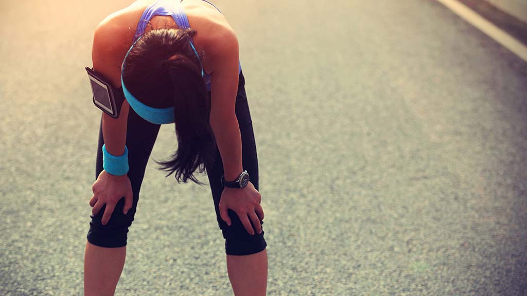 Woman with her hands on her knees after run on the road