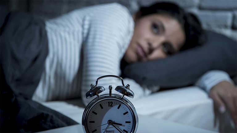 A woman unable to sleep lying in bed staring at her clock